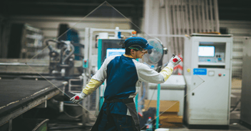Worker manually moving a glass tray in a factory, among production equipment.