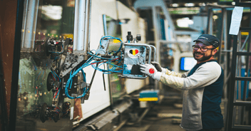 Operaio sorridente che aziona una macchina industriale in un ambiente di produzione.
