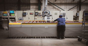 A worker on a production line looks at a computer screen displaying ERP software, surrounded by industrial machinery.