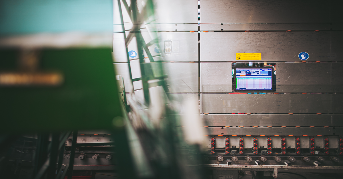 Vista di una vetreria con uno schermo a parete che mostra un ERP utilizzato per il monitoraggio della produzione in tempo reale.