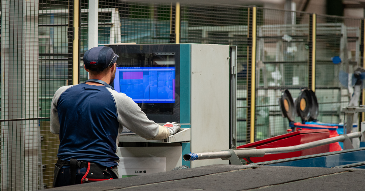Operaio industriale al lavoro su un PC che visualizza il software ERP, integrato nella sua postazione di lavoro sulla linea di produzione.