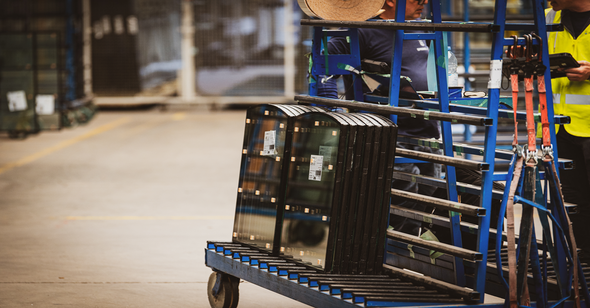 Glass transport racks loaded with small glass panels, lined up in an industrial space.